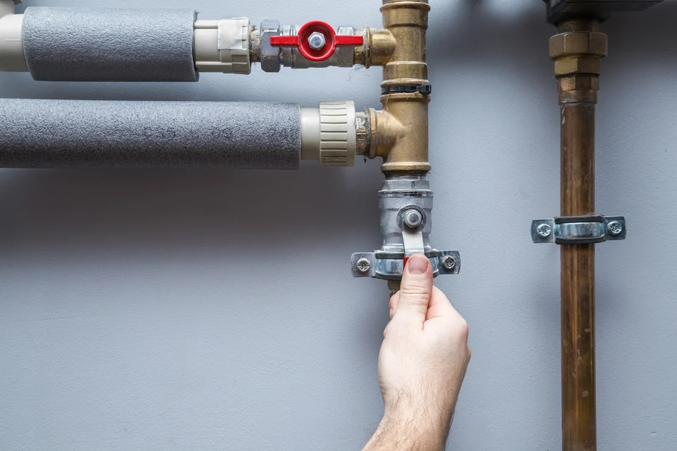 Main d'un technicien actionnant une vanne de coupure sur installation de plomberie murale