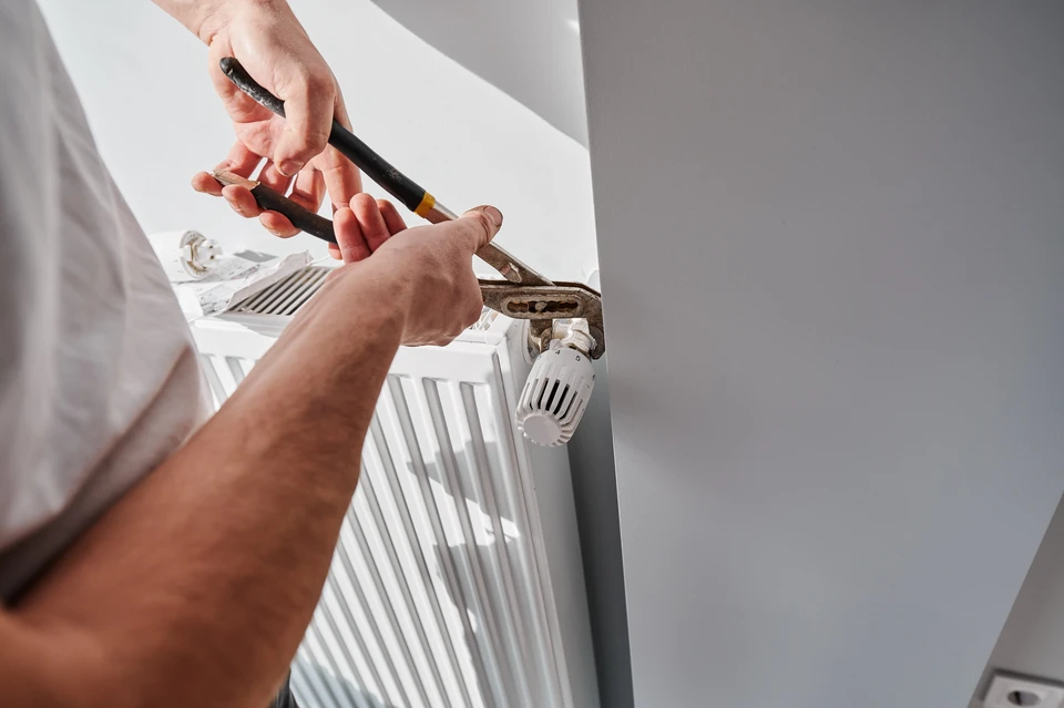 Technicien en plomberie travaillant dans une chaufferie résidentielle, ajustant une canalisation avec une clé à molette rouge